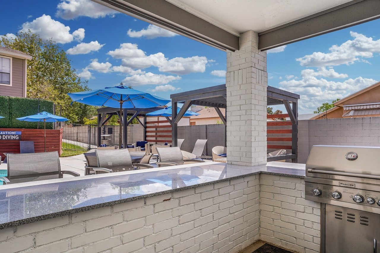 Outdoor community amenity area with grills, loungers, and blue umbrellas.