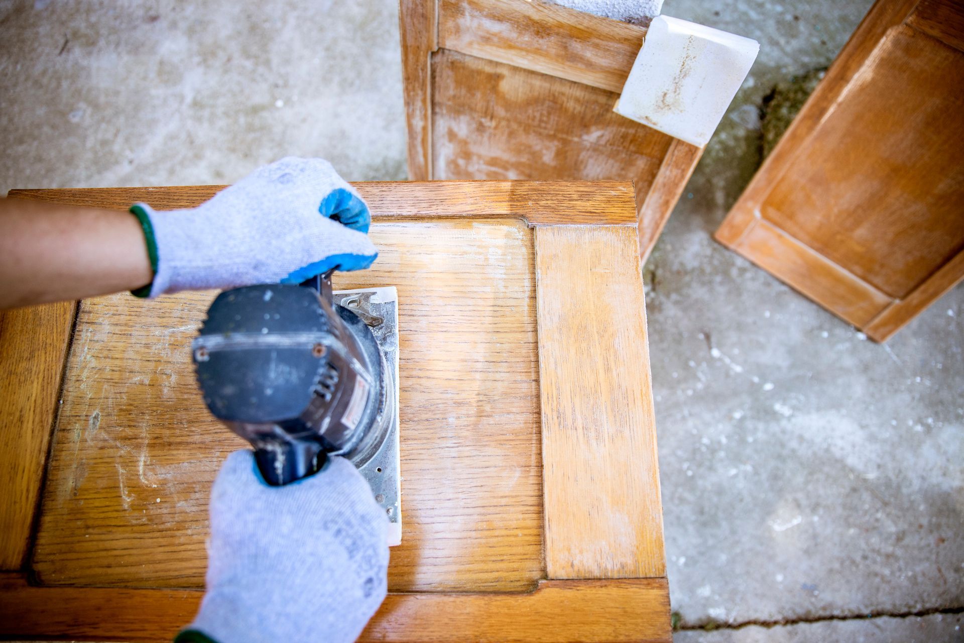 Man carpenter working with power sander tool on wood cabinet.