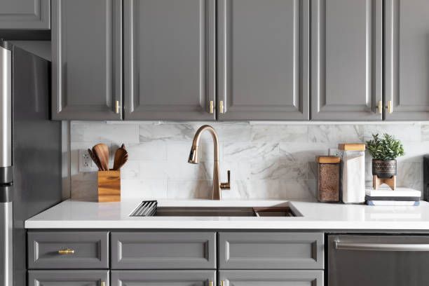 A kitchen with gray cabinets after cabinet refinishing, a marble countertop, and a backslash.
