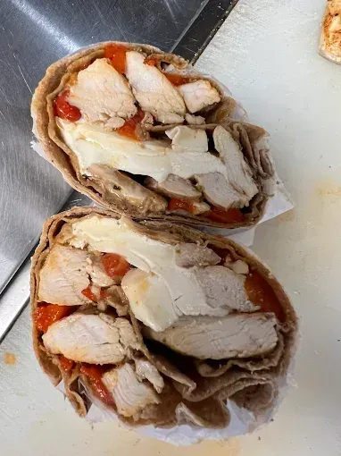 Chicken wrap cut in half, showing chicken, cheese, and red peppers in a wheat tortilla.