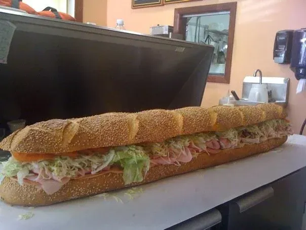 Long deli sandwich with various toppings on a counter, restaurant setting.