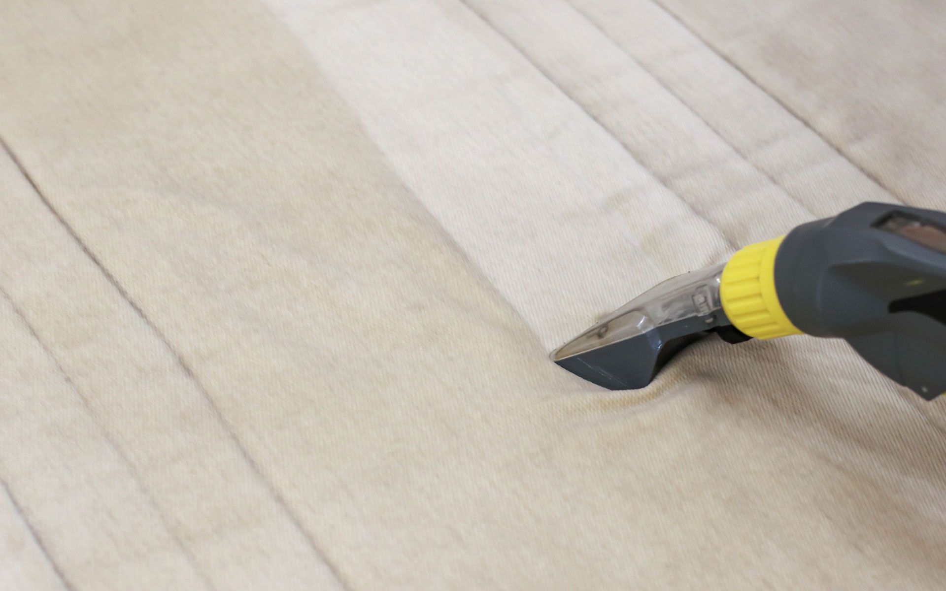 Steam cleaner head cleaning a light-colored, striped fabric surface.