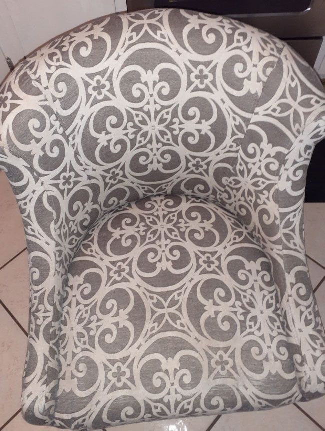 Person using a carpet cleaner on a gray upholstered chair.