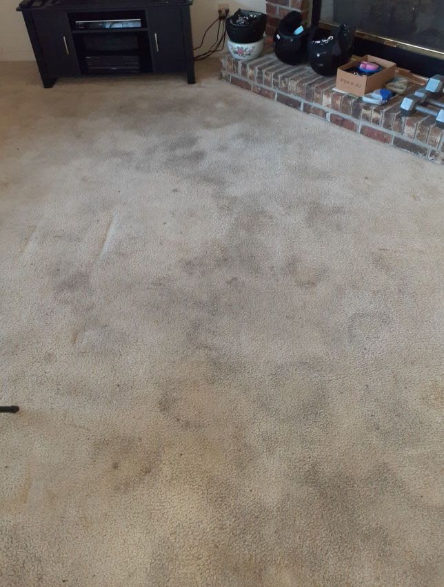 Beige carpet with dark stains, in a living room with a fireplace and entertainment center.