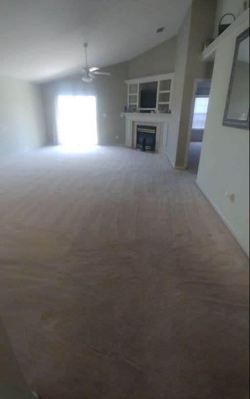 Empty living room with beige carpet, fireplace, and bright window.