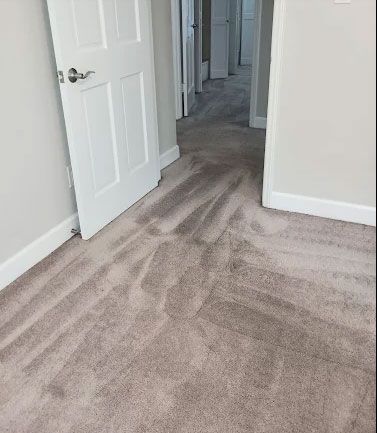 A hallway with light-colored carpet. A partially opened white door to the left. Other doors are visible down the hallway.