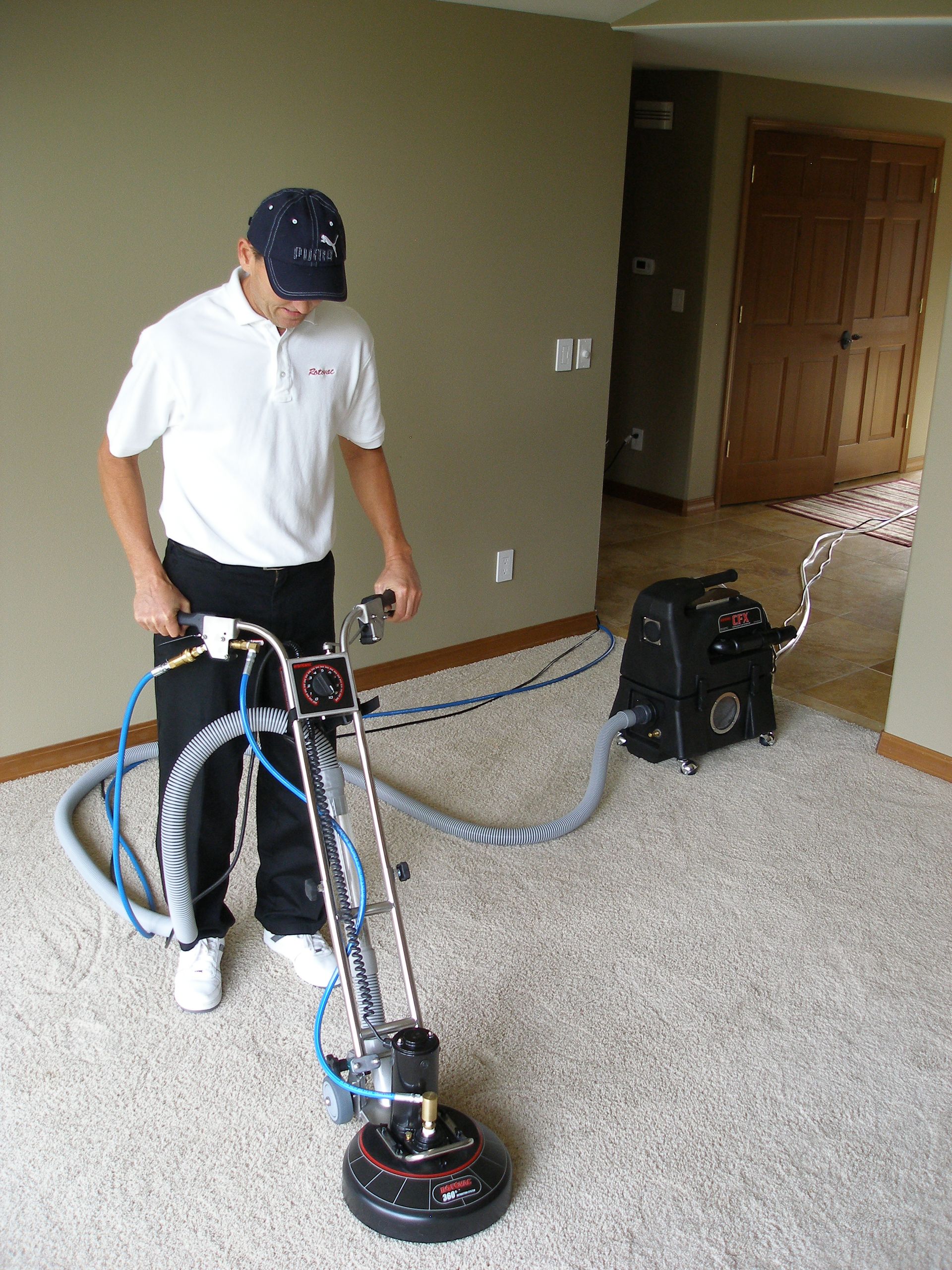 Person vacuuming a patterned rug with a carpet cleaner in a living room.