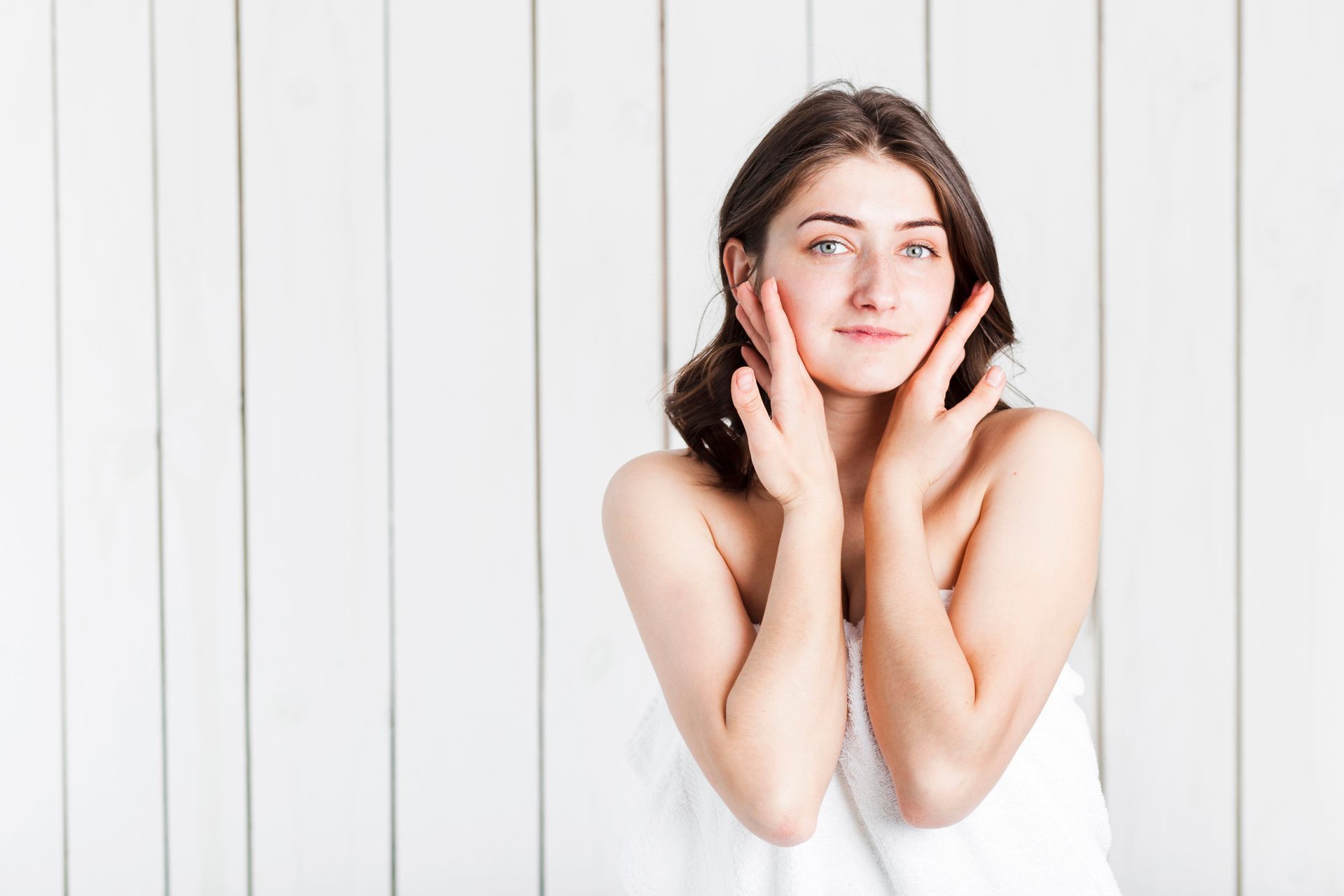 A woman is smiling while applying cream to her face.