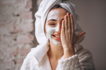 A woman with a towel wrapped around her head is wearing a facial mask.