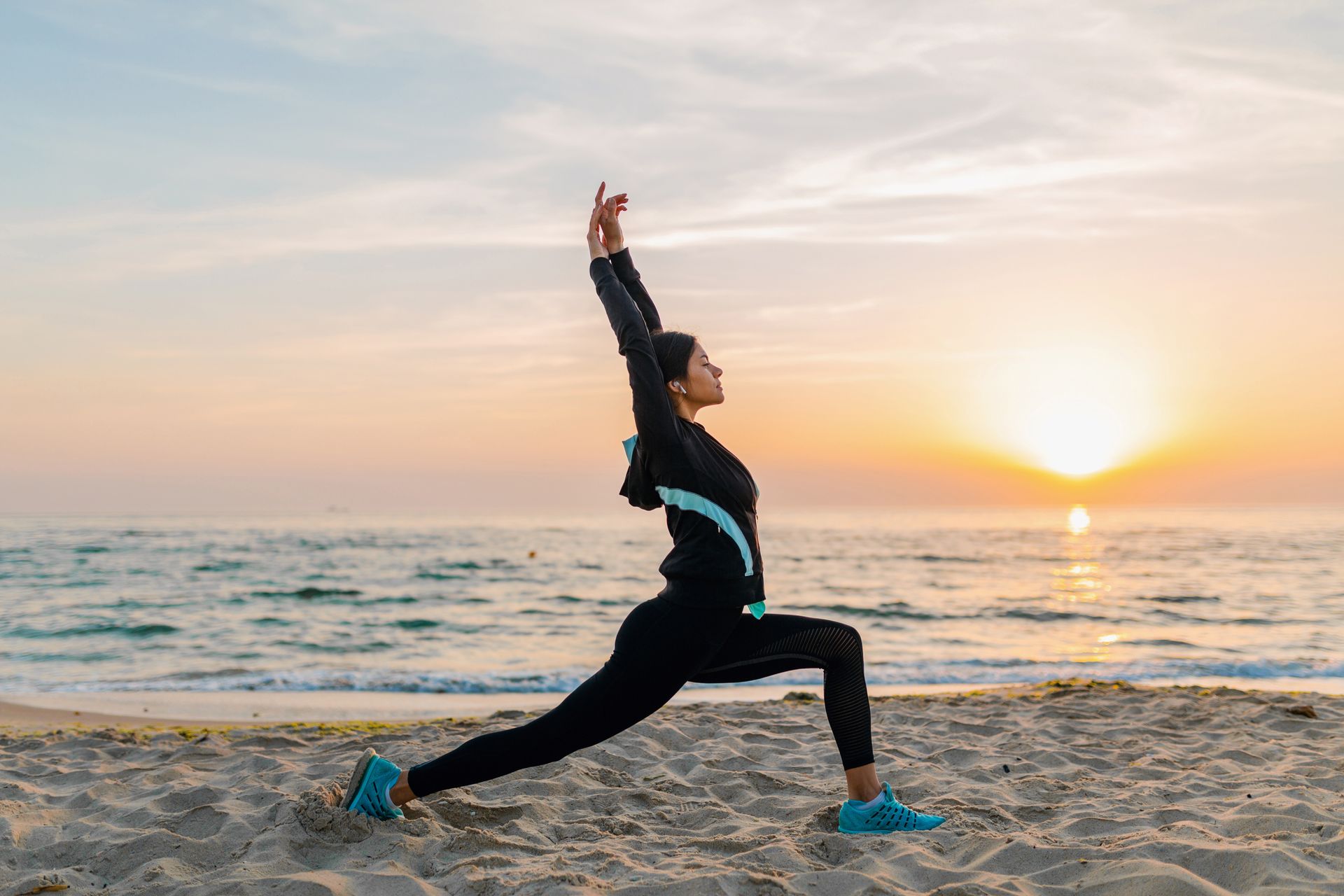 A woman is doing yoga on the beach at sunset.