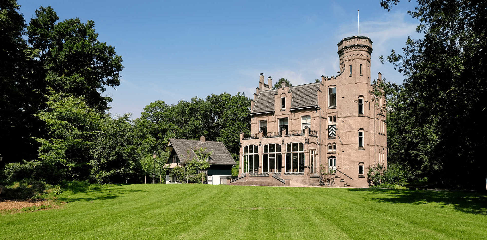 Een groot bakstenen gebouw met een toren midden in een weelderig groen veld
