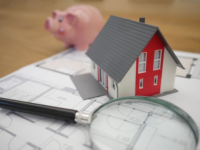 a piggy bank sits next to a magnifying glass and a model house