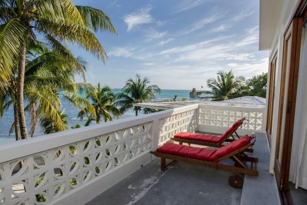 Balcony with ocean view; two red lounge chairs, palm trees, blue sky.