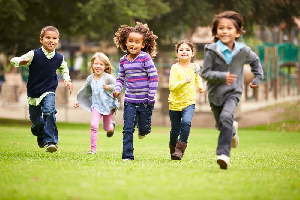 Group of young children running and smiling on a grassy field at a park on a sunny day