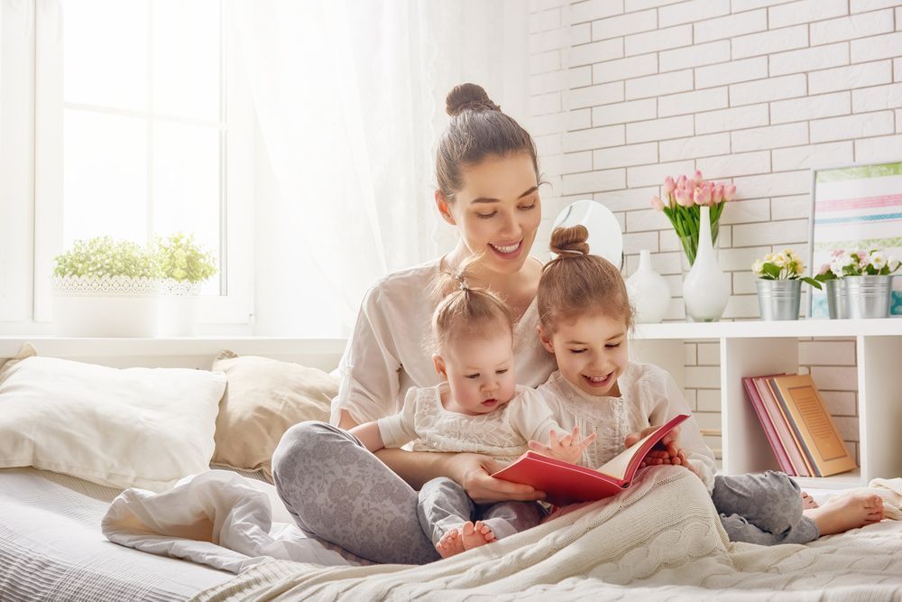 A Woman is Sitting on a Bed Reading a Book to Two Children — Woodlands Child Care Centre in East Albury, NSW
