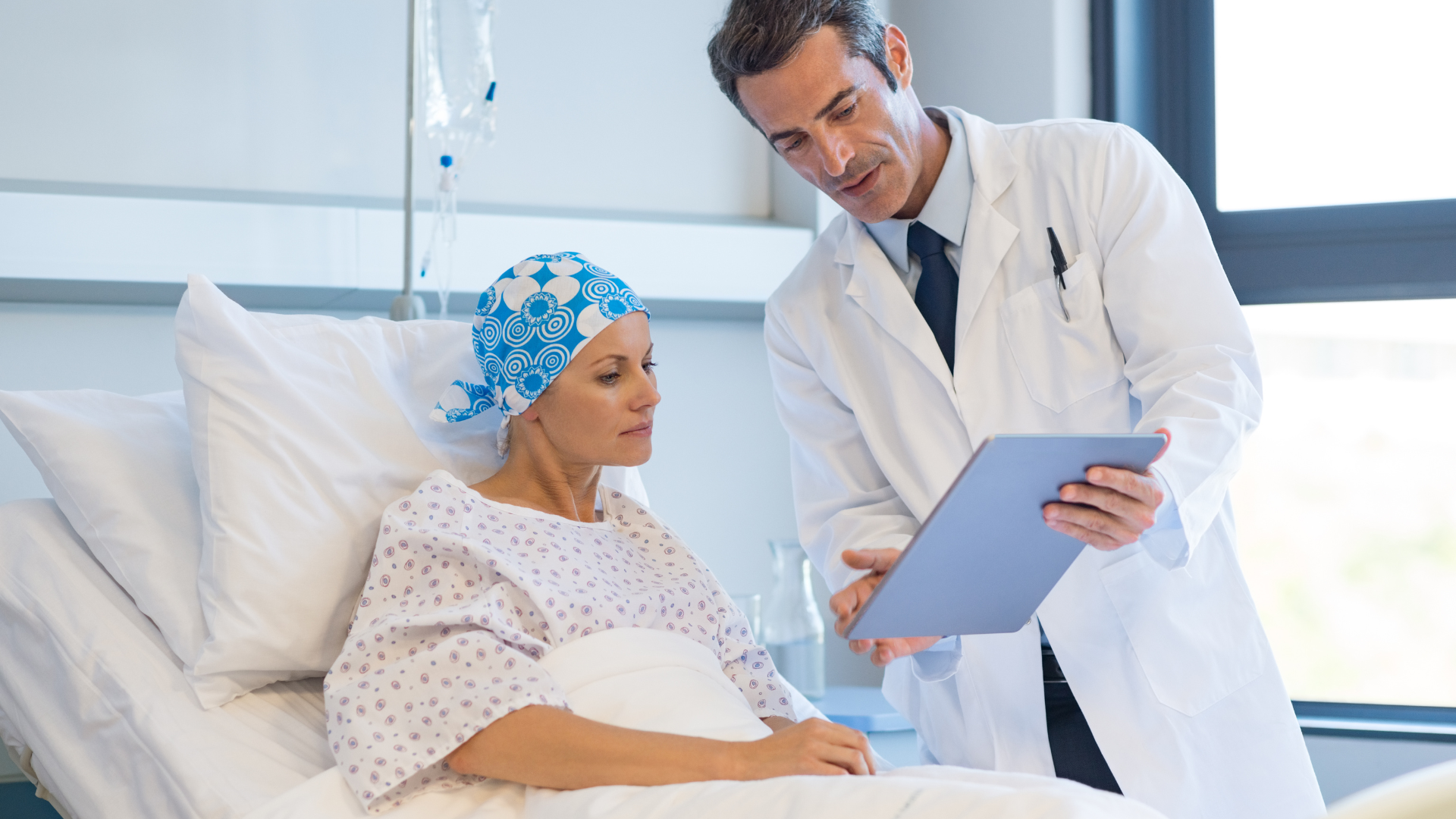 Doctor showing tablet to patient in hospital bed. Patient wearing headscarf.