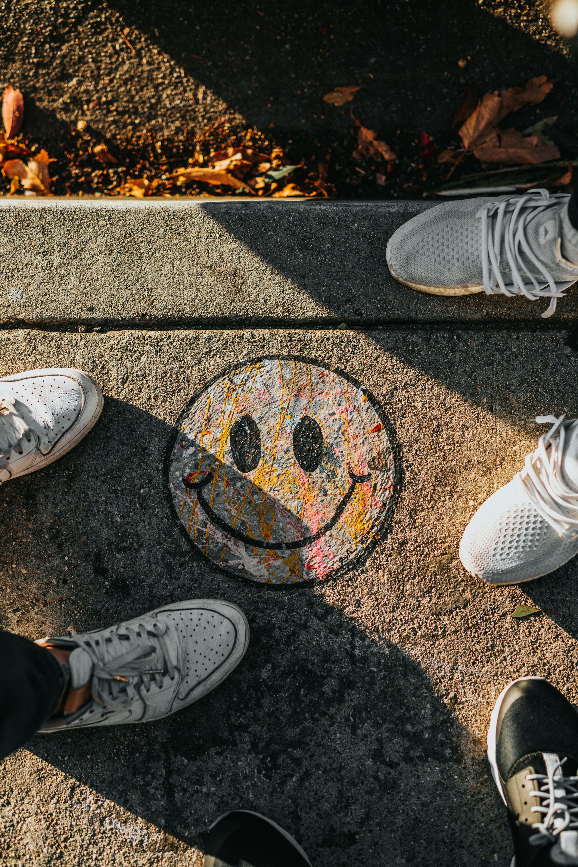 Smiley face painted on pavement, surrounded by feet in sneakers.