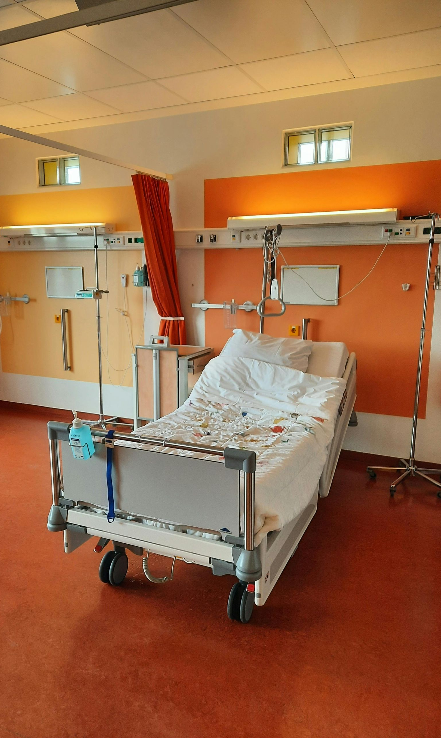 Hospital bed in a room with orange walls and medical equipment.