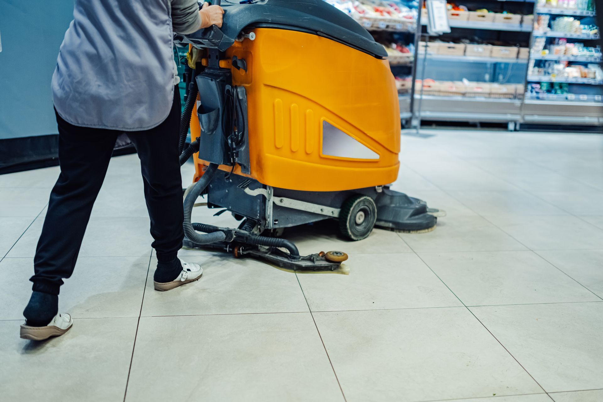 A person is cleaning the floor of a supermarket with a machine.