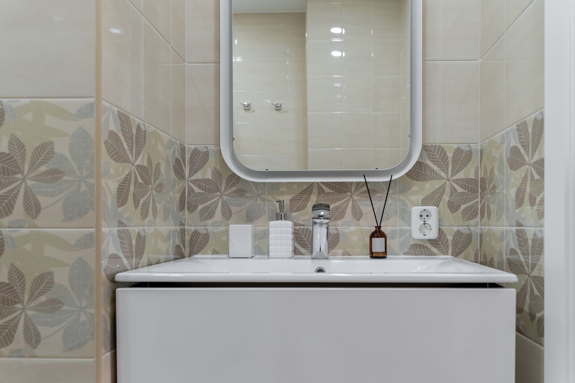 A bathroom with a sink , mirror and floral tiles.