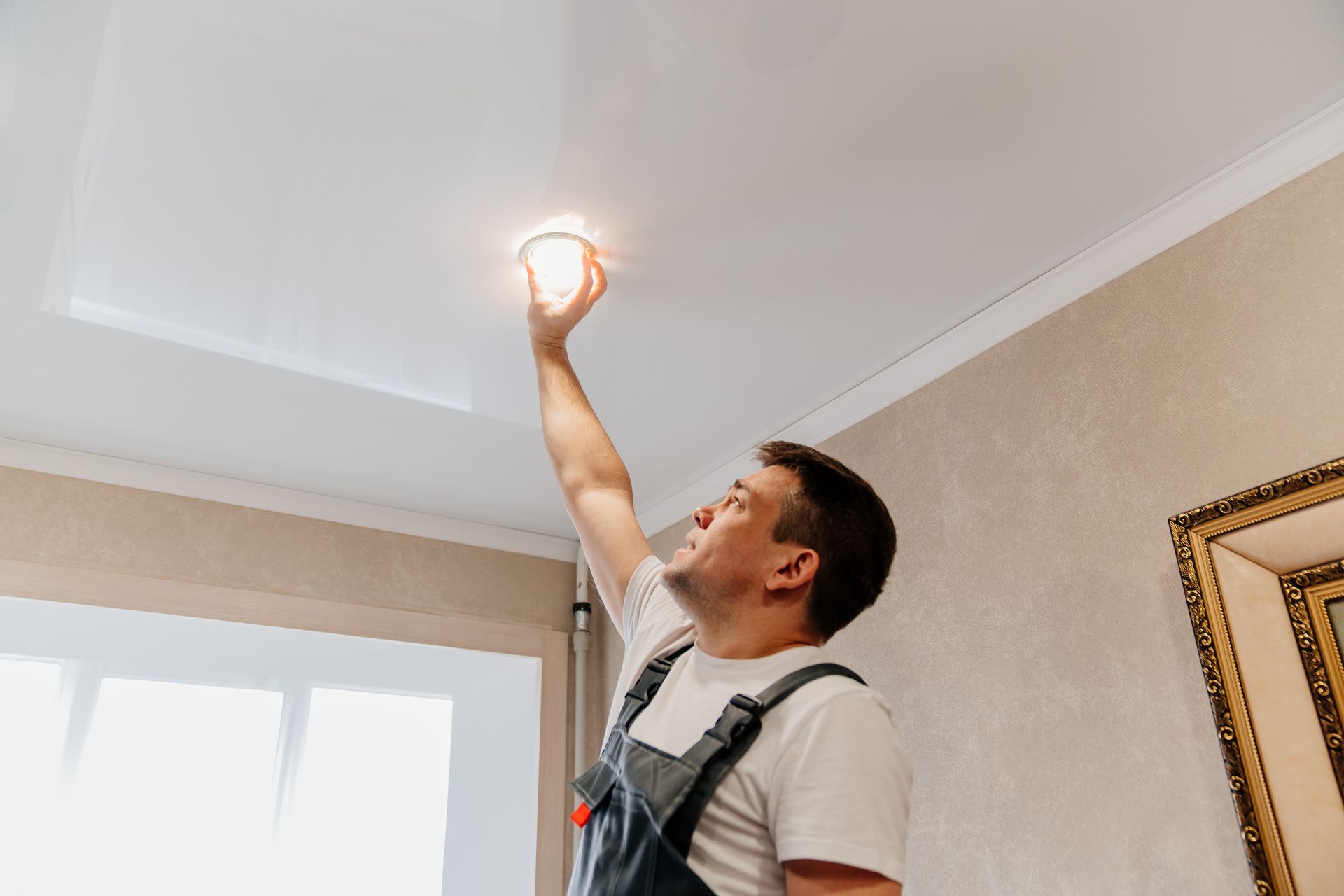 A man is changing a light bulb on the ceiling.