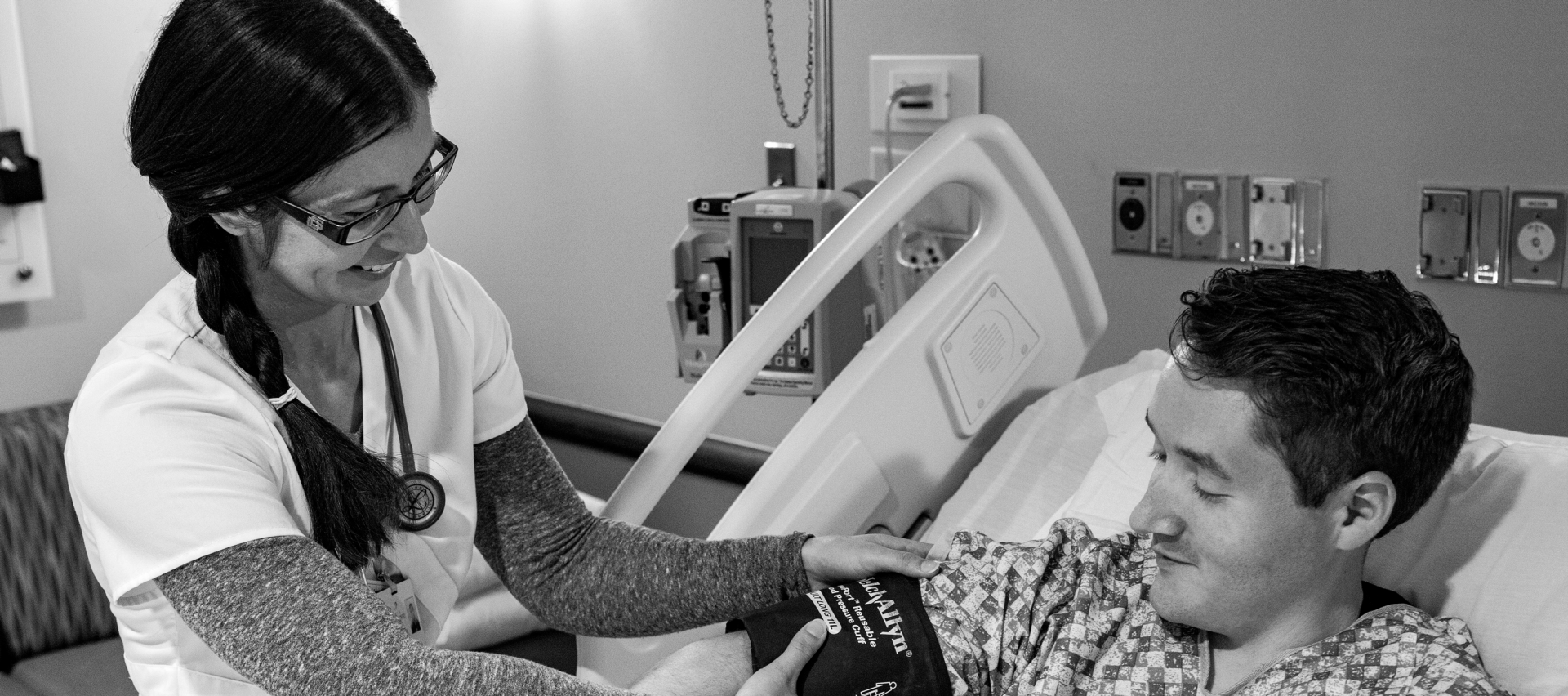 Kansas Surgery and Recovery Center's young female Nurse at bedside of a young male patient checking his blood-pressure