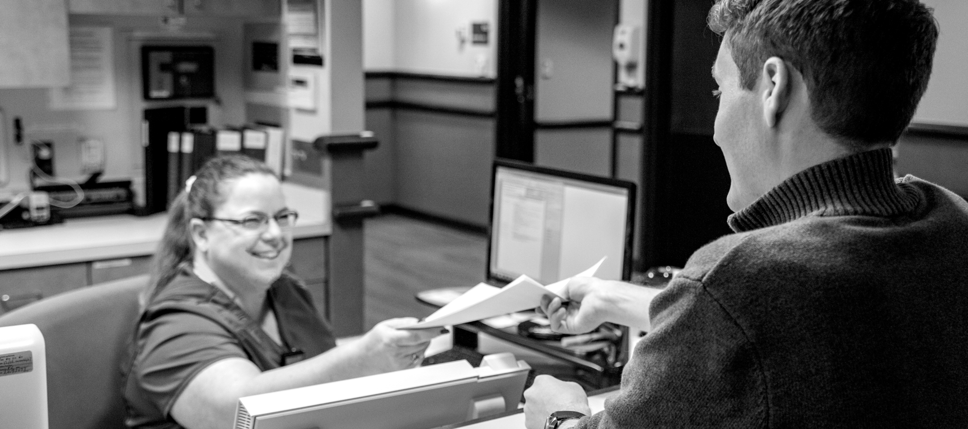 Kansas Surgery and Recovery Center's font desk assistant giving paperwork to young male at the front desk