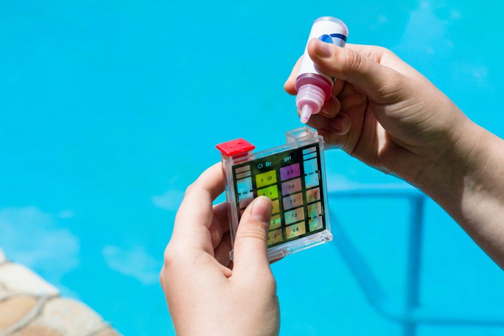 A Person is Holding a Test Kit in Front of a Swimming Pool — Tweed Coast Pool Care in South Murwillumbah, NSW