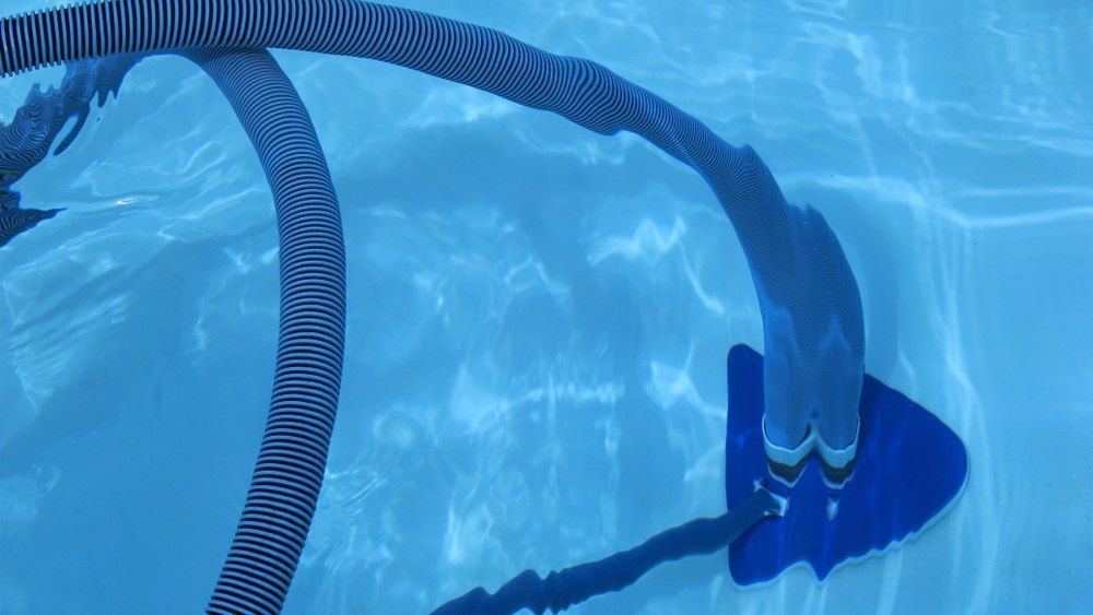 A Vacuum Cleaner is Cleaning the Bottom of a Swimming Pool — Tweed Coast Pool Care in Burringbar, NSW