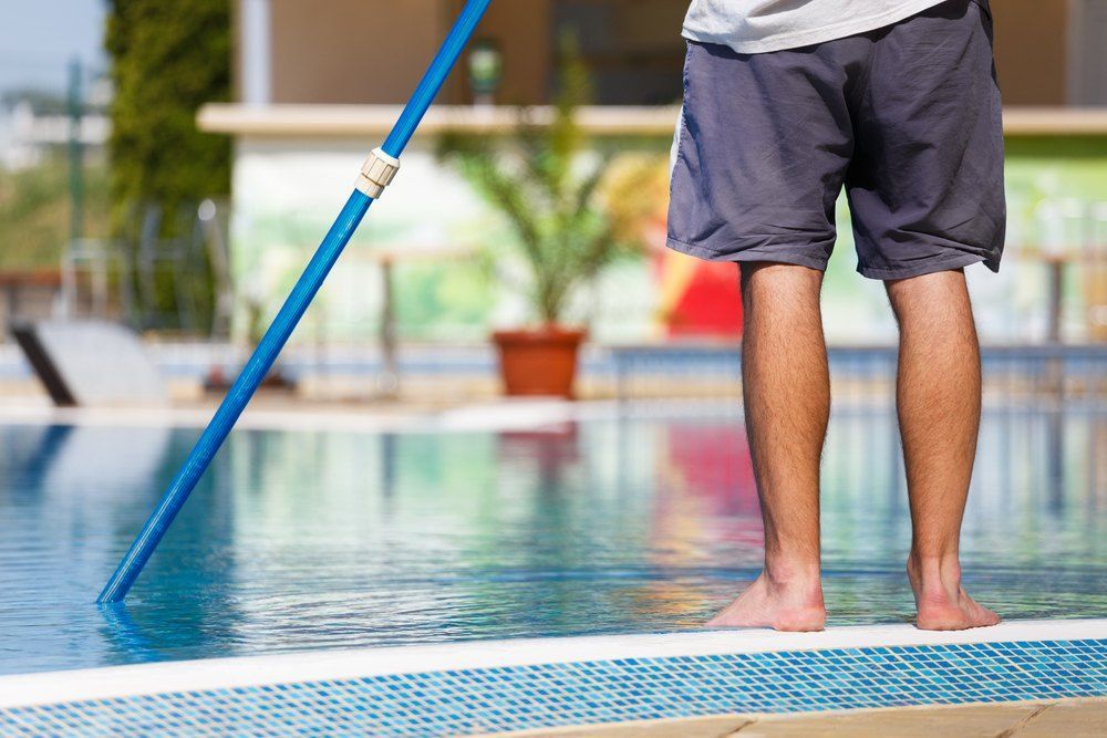 A Man is Cleaning a Swimming Pool With a Broom — Tweed Coast Pool Care in South Murwillumbah, NSW