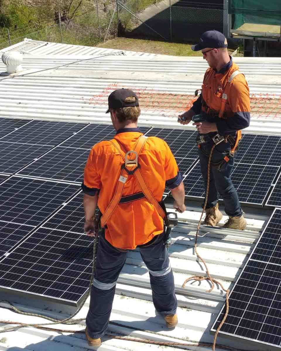 Two Men Are Working On A Roof With Solar Panels — CJ Electrical & Solar In Gorokan, NSW