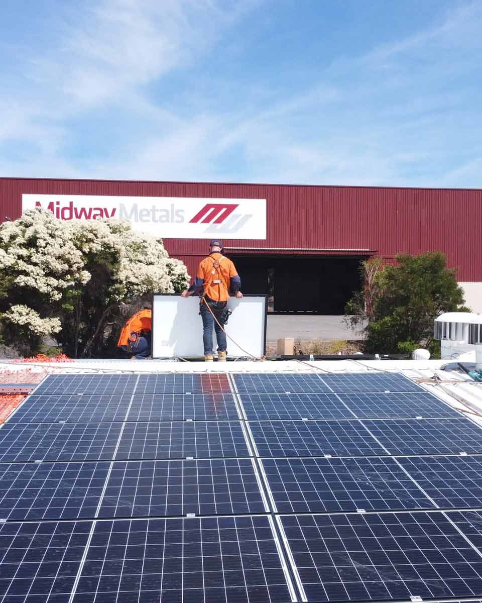 A Man Is Standing On Top Of A Solar Panel — CJ Electrical & Solar In Charlestown, NSW