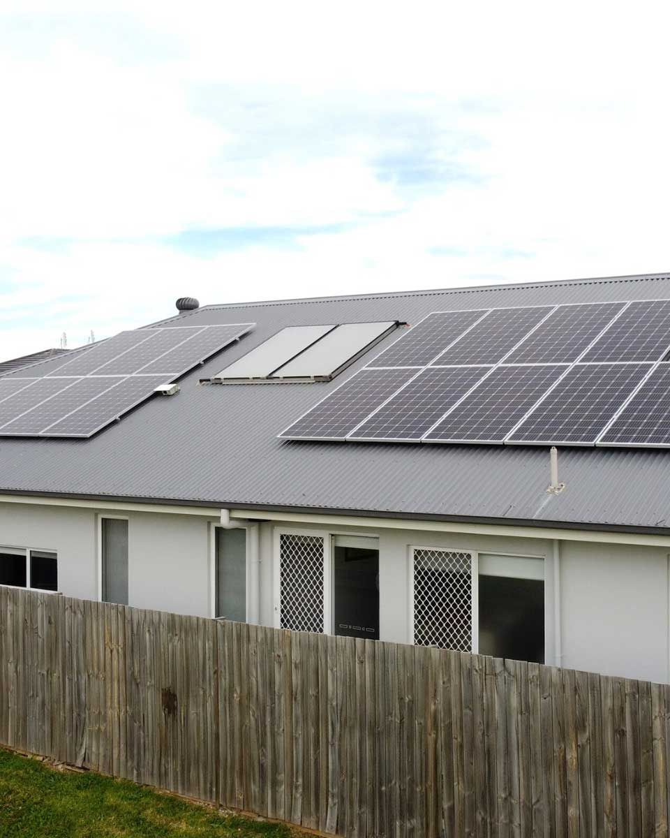 A House With Solar Panels On The Roof And A Wooden Fence — CJ Electrical & Solar In Mayfield, NSW