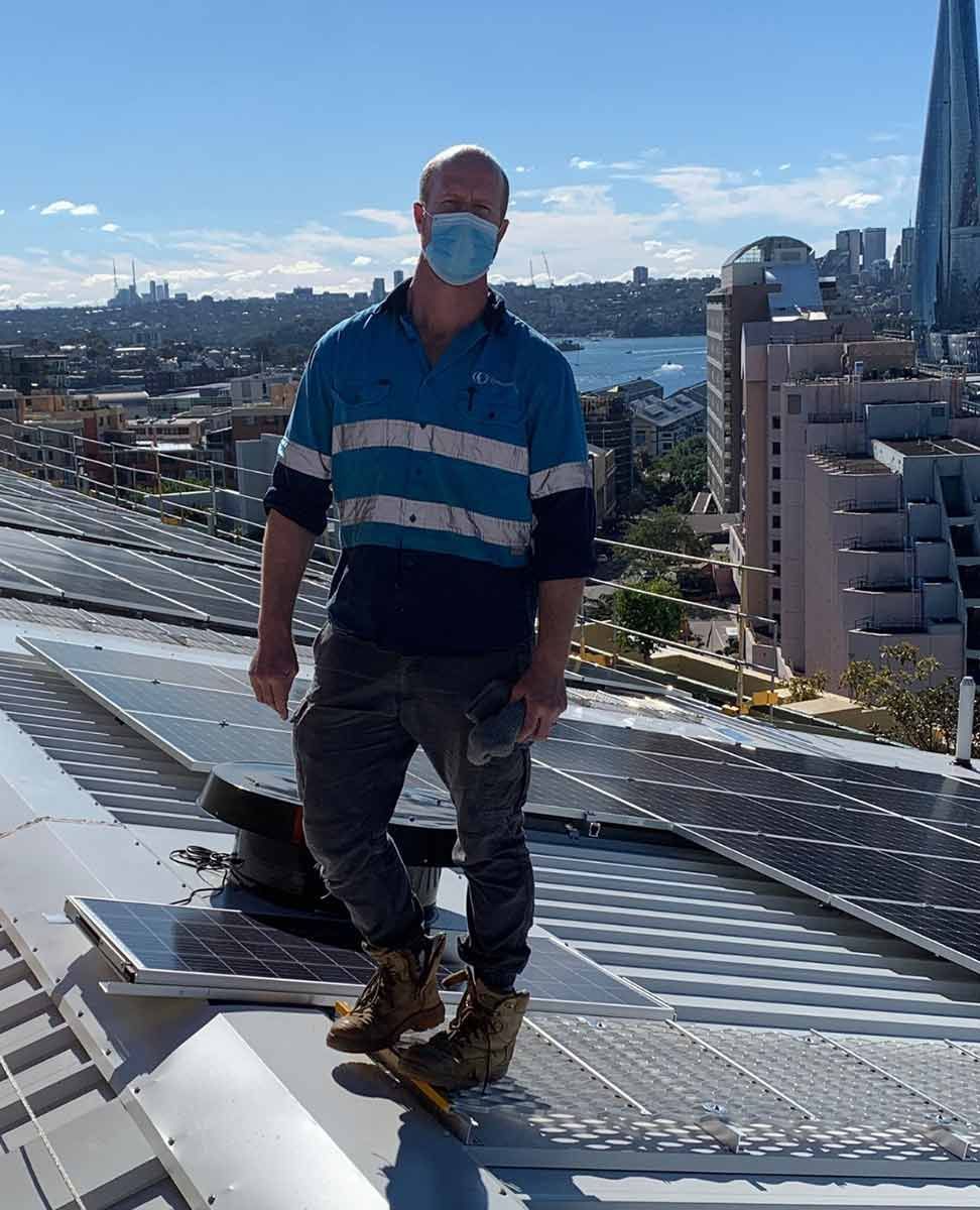 A Man Wearing A Mask Is Standing On The Roof Of A Building — CJ Electrical & Solar In Medowie, NSW