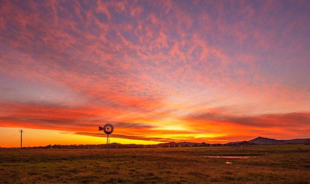 There Is A Windmill In The Middle Of A Field At Sunset — CJ Electrical & Solar In Aberglasslyn, NSW