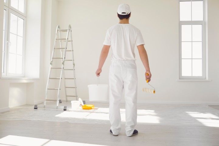A man is standing in an empty room holding a paint roller and bucket.
