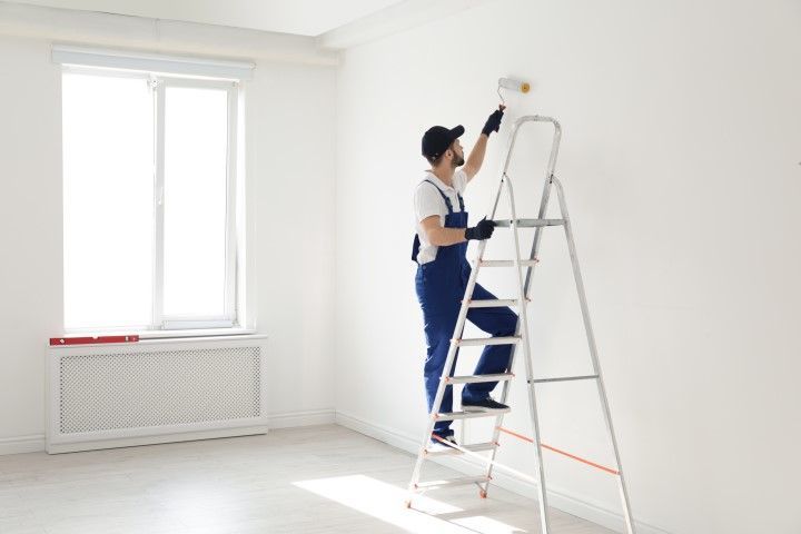 A man is standing on a ladder painting a wall.