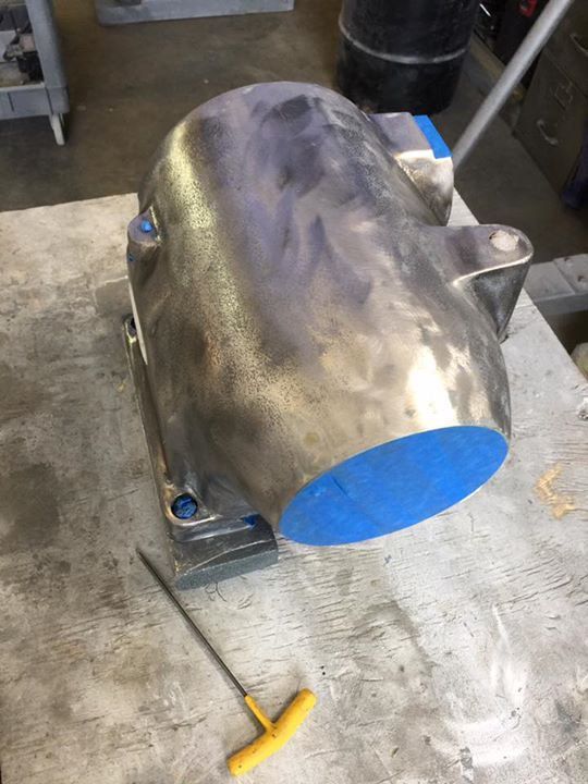 A metal object is sitting on a table next to a yellow wrench.