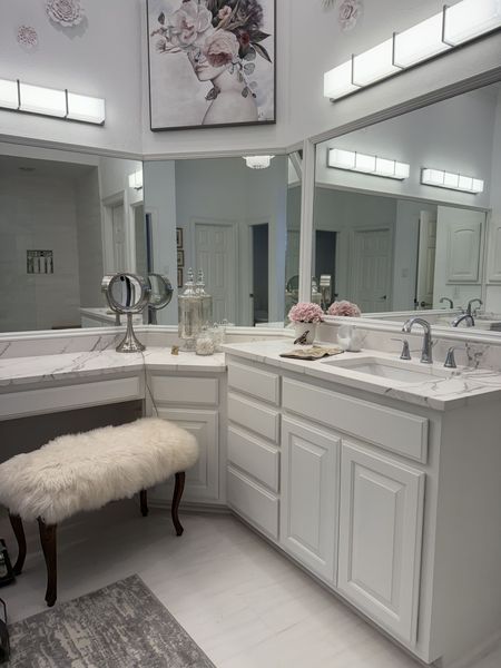 A bathroom with a vanity , sinks , mirrors and a bench.