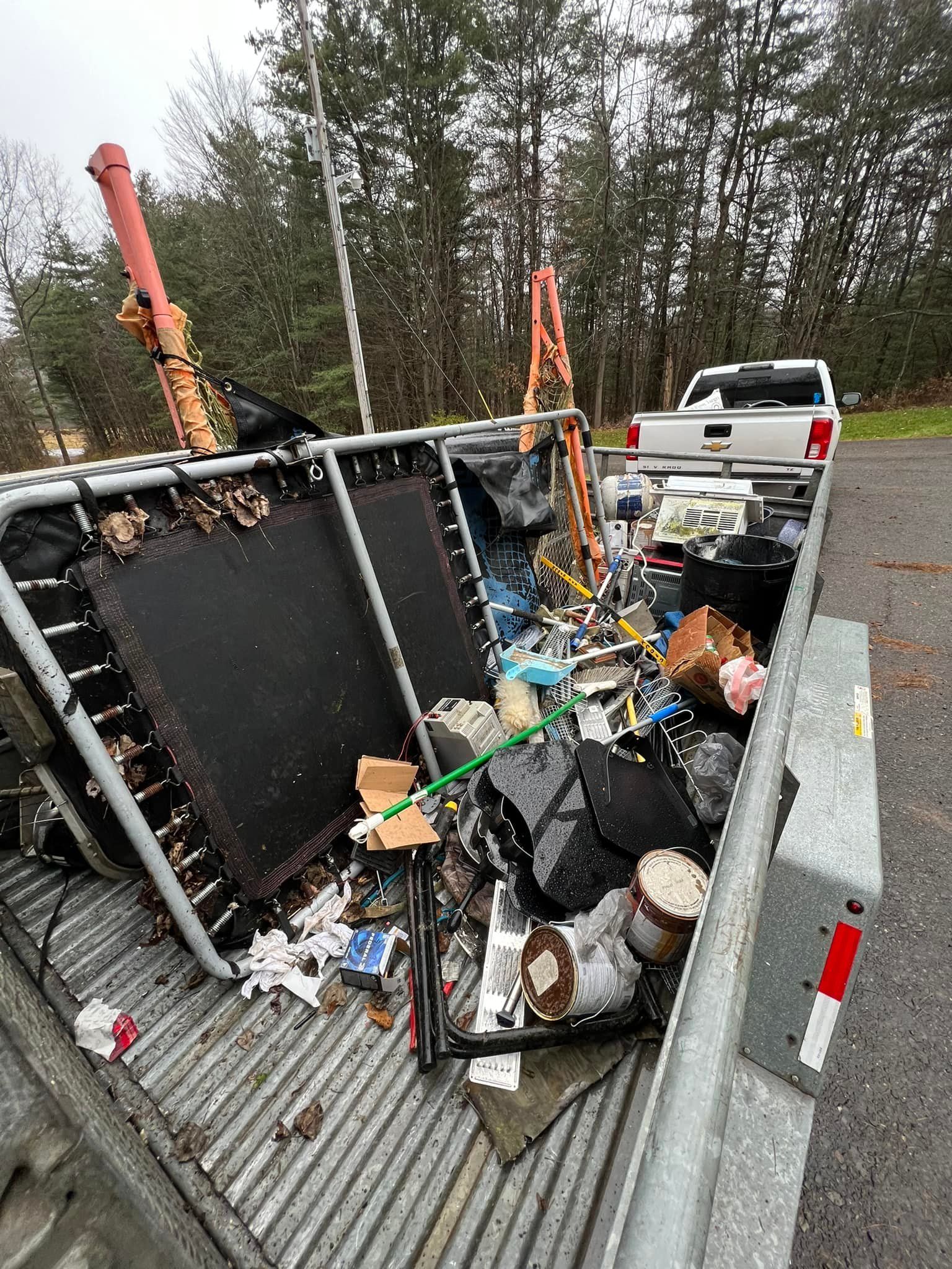 A truck bed overflowing with trash, including a trampoline and bags, parked on a road.
