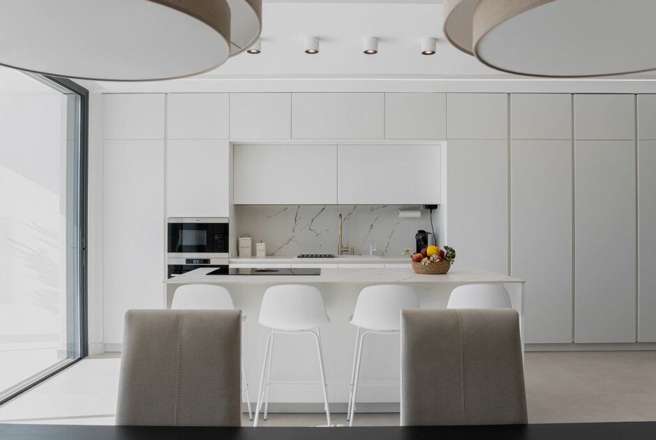 Una cucina con mobili bianchi, tavolo e sedie