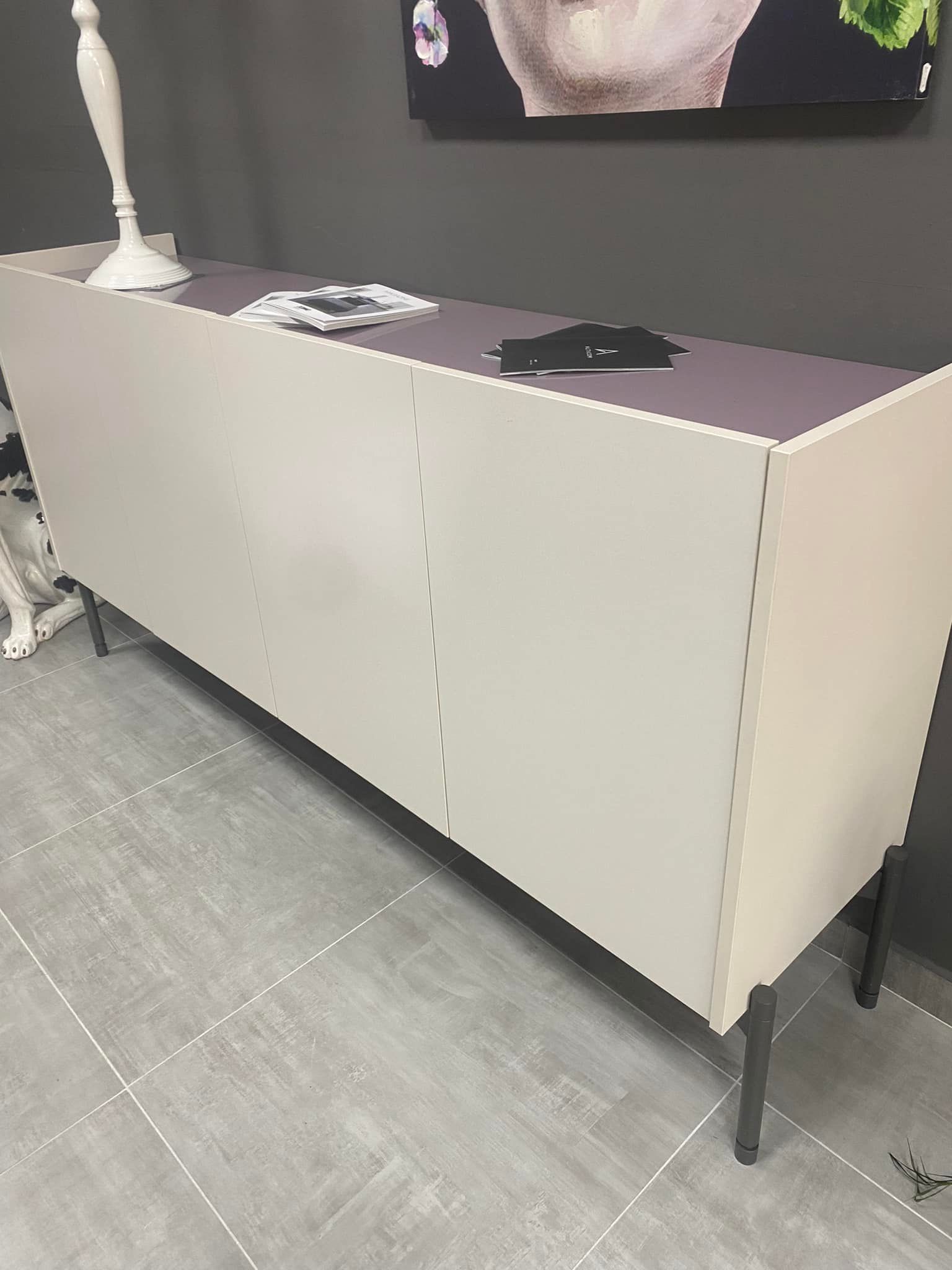 Una cassettiera bianca con il ripiano viola è appoggiata sul pavimento piastrellato di una stanza.