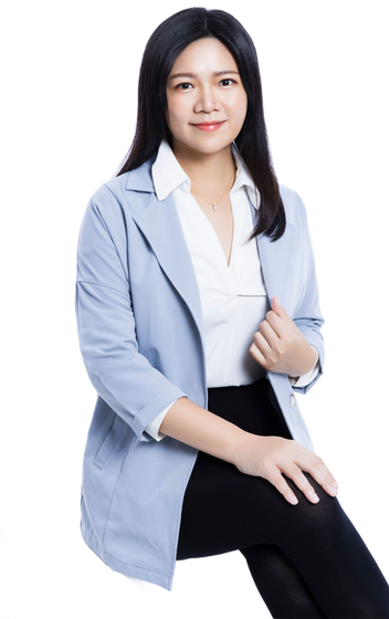 身穿藍色西裝外套、白色襯衫和黑色褲子的詠華地政士事務所所長-鄭秀慧女士,面帶微笑,坐著面對鏡頭。