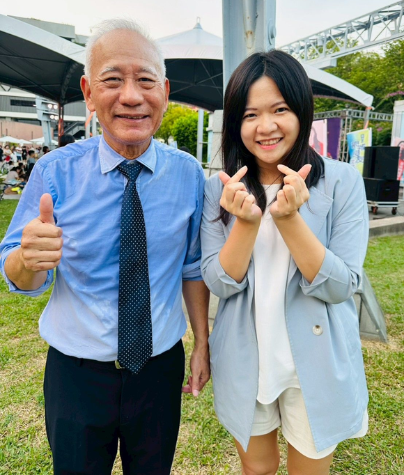 戶外,一名身穿藍色襯衫的男子豎起大拇指大力推薦,詠華地政士事務所所長-鄭秀慧女士在旁用手指比劃出愛心。
