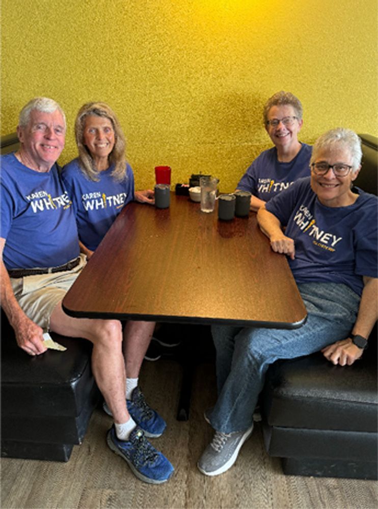 Four people wearing blue shirts with a name sit at a table in a restaurant.