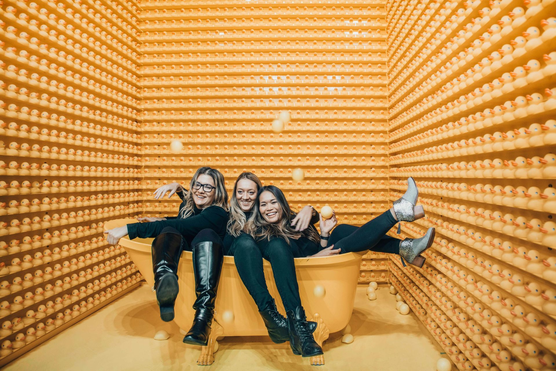 Three women are sitting on a bathtub in a room filled with ice cream cones.