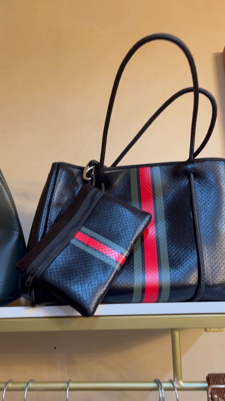 A black purse with a red and green stripe is sitting on a shelf.
