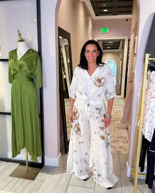 Woman in a white floral dress standing in a boutique hallway beside a green dress on display