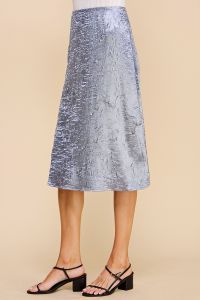 A woman is wearing a silver sequined skirt and black sandals.