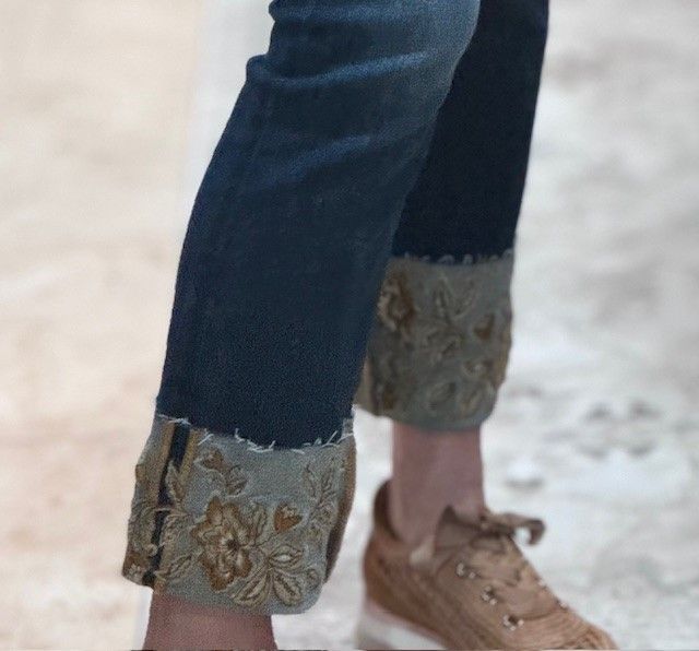 A person wearing a pair of jeans with embroidered cuffs